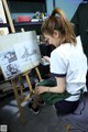 A woman sitting on a stool painting on a easel.