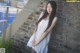 A woman in a white dress leaning against a brick wall.